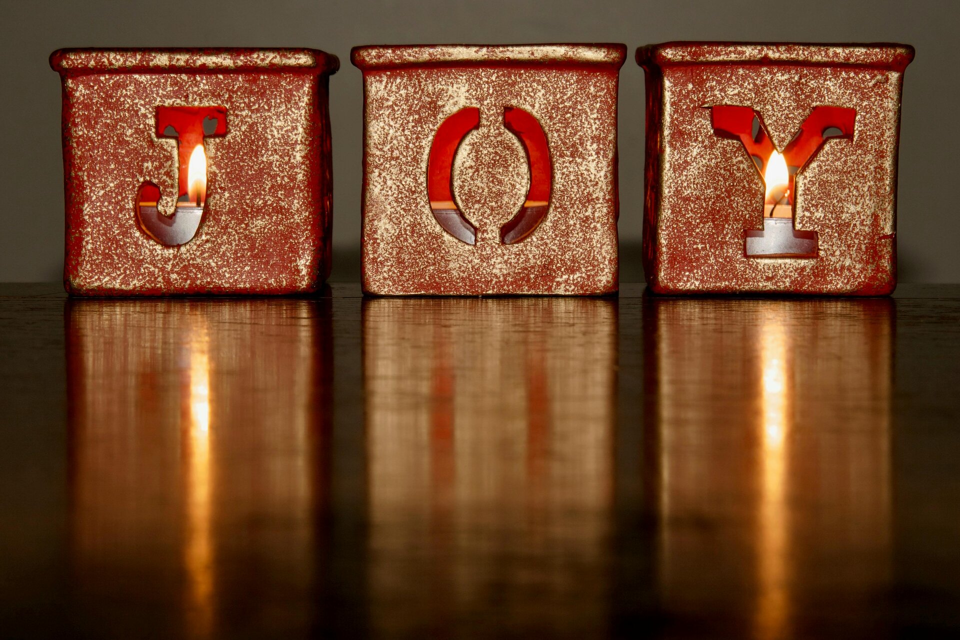 Three candle holders, each with letter cut out of the side, so that it spells "JOY"