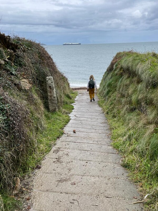 Woman walking down some steps towards a beach with the sea shown in the background
